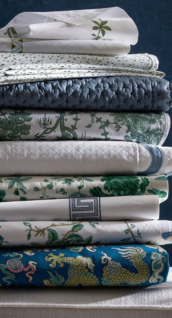 Assortment of Matouk Schumacher bedding folded on the ladder steps.